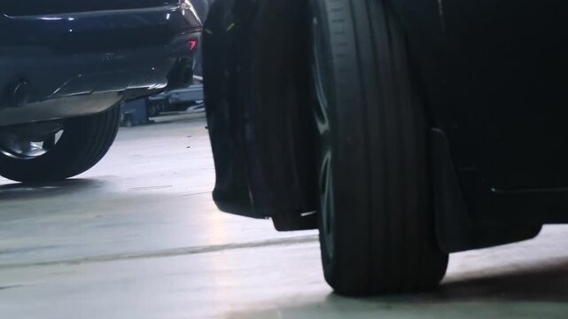 Modern car wheel turns while vehicle drives out of service station closeup. Automobile with titan hubcap leaves garage lit by led light