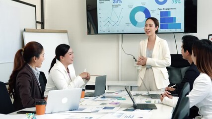 Female executive leading strategic team meeting, presenting data driven insights on large screen while fostering collaborative professional discussion in modern corporate environment