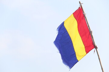 Romanian flag with vertical blue, yellow, and red stripes waving on a pole against a clear sky. Ideal for national, cultural, travel, or identity-themed visual content