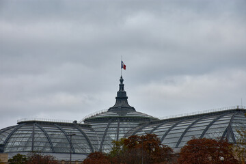 Dome of the Grand Palais in Paris with an iron and glass structure and a waving French flag under a cloudy sky