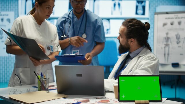 Licensed doctor and his staff review x ray scan results next to isolated copy space screen, examining hospital records before putting a diagnosis. Consulting analytics and radiography. Camera B. - Powered by Adobe