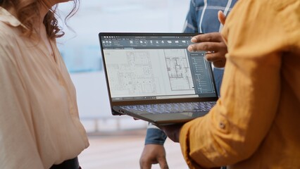 Real estate agent advising clients on office relocation and leasing, reviewing detailed blueprints and discussing the architectural design of the new property. Contract negotiation. Camera B.