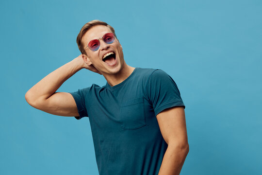 smiling man wearing casual teal t-shirt and round sunglasses look camera enjoy digital detox lifestyle concept isolated on blue background