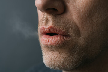 Fototapeta premium Close up of middle aged man exhaling breath in cold air with chapped lips and stubble on his face