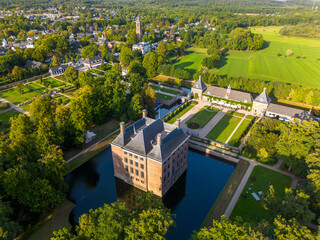 Aerial view of historic moated castle with gardens, bridge, and adjacent long building, surrounded...