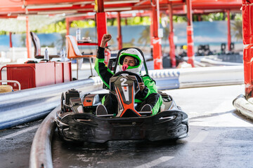 Woman in helmet and racing suit raising her fist on a go kart track, celebrating triumph in a...