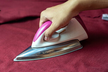 Close-up of a hand ironing a red fabric with a modern electric iron, showing household chores, clothing care, and fabric maintenance concept