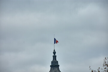 French flag flying at half-mast over the Grand Palais in Paris with a gray sky and metal architecture in the background