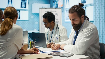 Physician writing a prescription for treatment plan at his cabinet desk, recommending medicine for disease prevention. Medic consulting analytics and hospital records in a clinic. Camera B.
