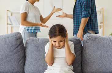 Sad child holding hands to ears to cover and ignore parents quarrel and conflict at home. Unhappy girl in needs safety and care, kid feeling fear, stress and trauma from adults arguments and shouting