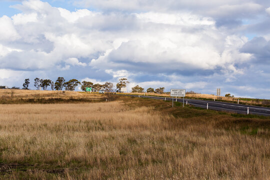 Grassy paddock on roadside with sign for overtaking lane keep left unless overtaking