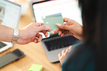 A person hands a payment card to another person over a laptop, symbolizing a transaction or financial exchange in a modern setting.