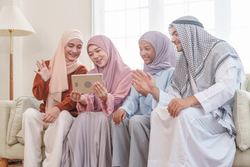 portrait of happy muslim family in traditional clothes sitting on sofa in living room at home,enjoying tablet together,family holiday leisure time