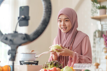 young beautiful muslim woman in hijab prepare organic fruits and vegetables for cooking on video live streaming in the kitchen,concept healthy food,technology,new marketing