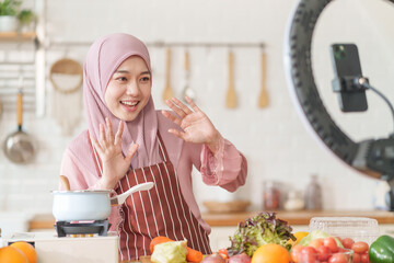 young beautiful muslim woman in hijab prepare organic fruits and vegetables for cooking on video live streaming in the kitchen,concept healthy food,technology,new marketing