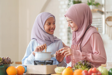 muslim girl with mother in hijab cooking organic vegetables and fruits together in the kitchen