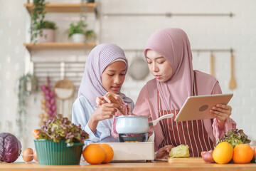 muslim girl and mother in hijab prepare organic vegetables and fruits, together with learning on digital tablet while cooking food in the kitchen