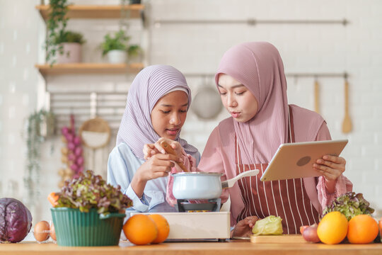 muslim girl and mother in hijab prepare organic vegetables and fruits, together with learning on digital tablet while cooking food in the kitchen