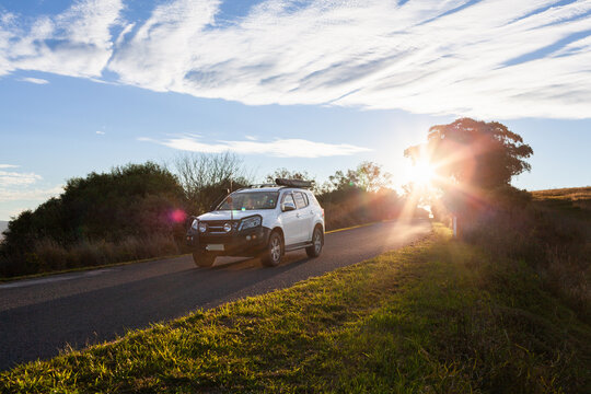 Car traveling down rural road with starburst of sunset light in rural Australia