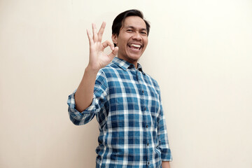 Fototapeta premium Southeast Asian man wearing flannel shirt cheerful expression and give oke gesture hand, on white isolated background