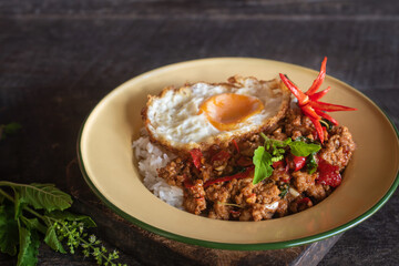 Beautifully presented stir-fried pork with basil and a fried egg, served in a vintage style plate garnished with fresh chilies, cucumber and herbs,.