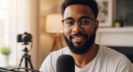 Confident African American man with glasses recording a podcast in a home studio. Male content creator and vlogger speaking into a microphone while looking at the camera