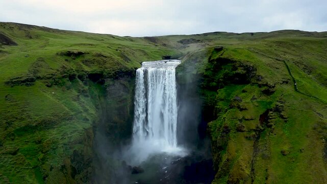 Witness the breathtaking Skogafoss Waterfall as it tumbles dramatically over green cliffs, surrounded by lush landscapes and a serene atmosphere, capturing the beauty of Icelands nature.