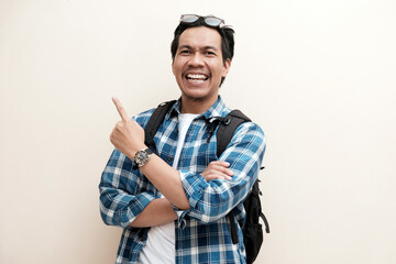 Southeast Asian man wearing cap and carrying backpack pointing to the right side with excited expression, vacation, holiday.