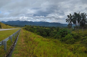 Idyllic landscape of mountain range in Negeri Sembilan, Malaysia with coconut trees and cloudy skies taken in Temiang Pantai route.