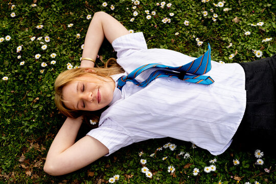 Teenage girl with a blue tie lying on grass field with tiny white flowers