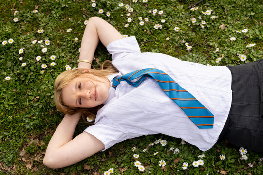 Teenage girl with a blue tie lying on grass field with tiny white flowers