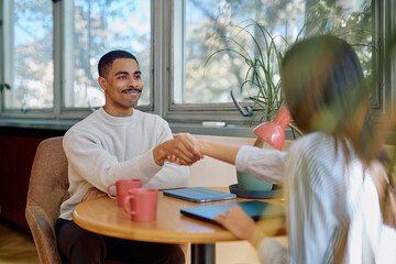 Diverse business partners shaking hands, finalizing a deal at a table in a modern office. Positive outcome, success concept