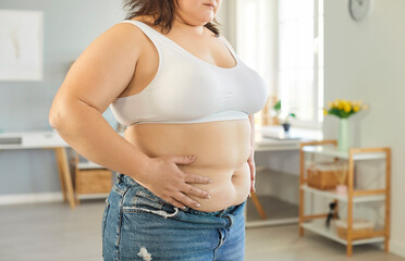 Fototapeta na wymiar Close up cropped view of plus size woman standing at home, holding her waist with her hands. Overweight female touching stomach, showing body insecurity, health concerns and focus on weight loss. Fototapeta na wymiar Close up cropped view of plus size woman standing at home, holding her waist with her hands. Overweight female touching stomach, showing body insecurity, health concerns and focus on weight loss.
