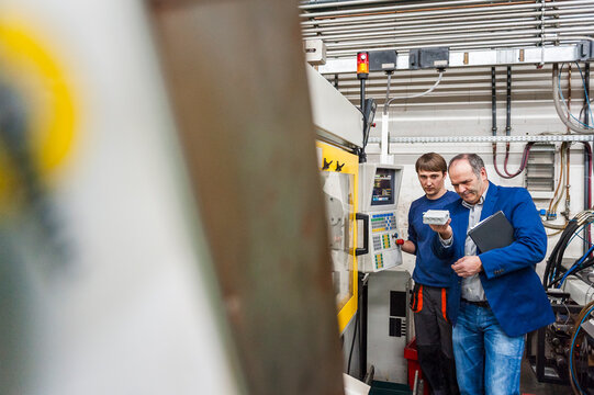 Manager and employee inspecting machine in plastics production hall