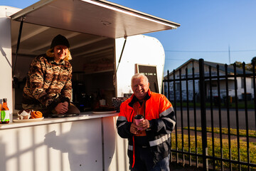 happy older Aussie workman in high vis workwear buying warm takeaway coffee from van