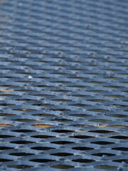 A low-angle, shallow depth of field shot capturing a wide area of dark, expanded metal mesh forming a floor or platform.
