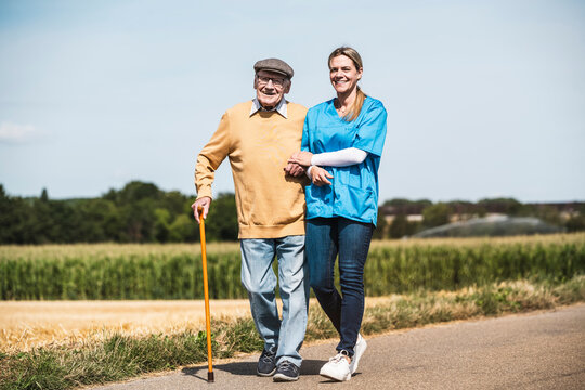 Smiling nurse walking with elderly man on road in front of clear sky