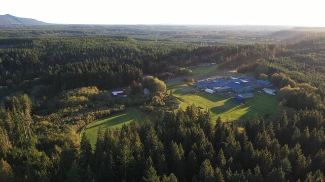 4K aerial drone footage of Lake Quinault School District area in Amanda Park, Washington State, USA, captured at sunset with warm golden light over surrounding evergreen forests and rural landscape