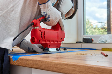 repairman using electric jigsaw and cutting hole for the sink in the kitchen countertops,...
