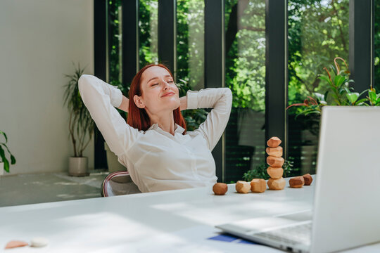 Smiling businesswoman with hands behind head relaxing in office