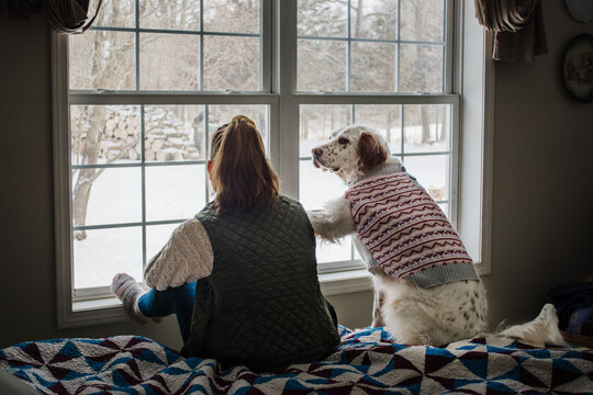 A girl and her dog looking out the window at the snow
