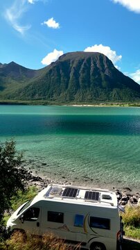 Explore the serene beauty of Lofoten, Norway, where a cozy camper van sits by clear blue waters surrounded by impressive mountains. A camper van camps at the ocean front