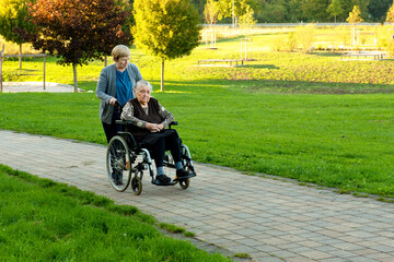 Caretaker in blue uniform taking a walk with elderly female patient through park with help of...