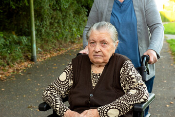 Caretaker in blue uniform taking a walk with elderly female patient through park with help of...
