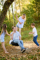 Family enjoys playing outdoors, with father sitting on homemade tire swing, mother standing behind...