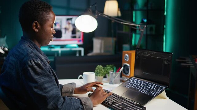 Teleworker in living room office using laptop to do coding for software developing, handheld camera shot. Remote employee typing on device keyboard, solving tasks in apartment, camera B close up