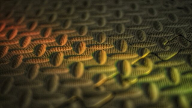 Non-slip rubber mat with oval tread pattern under colored light, industrial surface texture macro