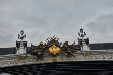 Sculptural detail of the Pont Alexandre III in Paris with golden figures and the imperial emblem against a cloudy sky