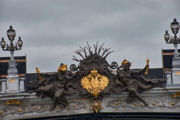 Sculptural detail of the Pont Alexandre III in Paris with golden figures and the imperial emblem against a cloudy sky