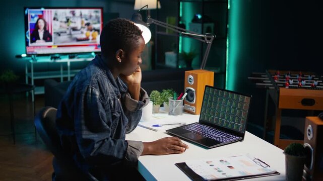 Self employed broker investor in home office checking stock exchange profit on laptop device. African american freelancer in apartment looking at market shares growth on notebook, camera B